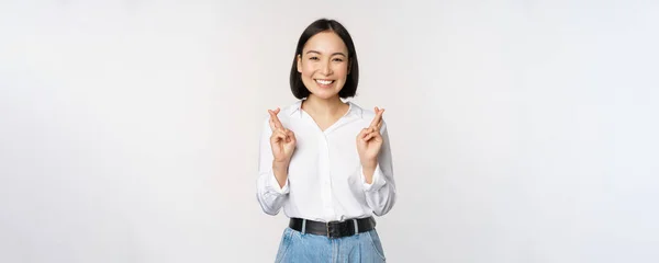 Retrato de mujer joven coreana, chica asiática cruzan los dedos y rezan, pidiendo deseo, anticipando, esperando resultados, de pie sobre fondo blanco — Foto de Stock