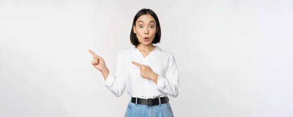 Retrato de mujer asiática joven excitada, señora de la oficina señalando los dedos a la izquierda en el descuento, mostrando banner de venta, de pie sobre fondo blanco —  Fotos de Stock