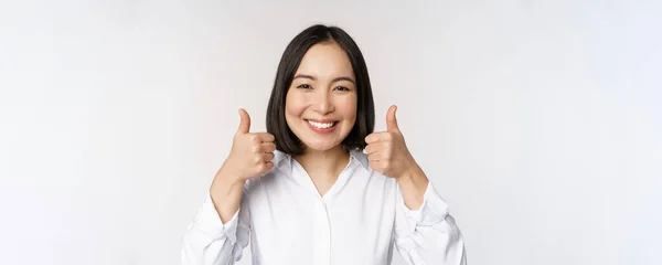 快乐的亚洲女人的脸，竖起大拇指笑着，为某事感到高兴，推荐闻起来不错，站在白色的背景上 — 图库照片
