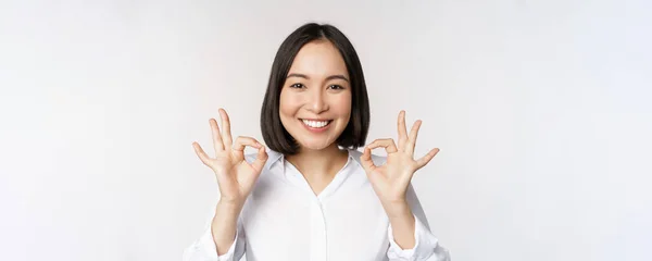 Close up head portrait of asian girl showing okay, ok sign and soring satisfied, recommending, being pleased, praise and make compliment, white background — Fotografia de Stock