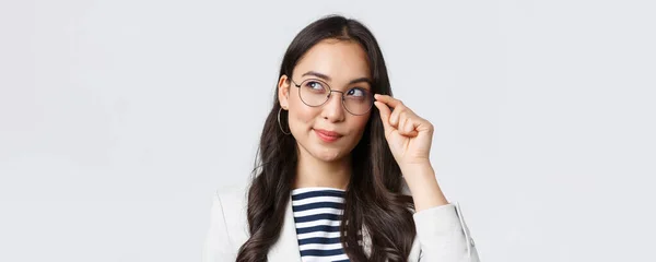 Negócios, finanças e emprego, conceito de empresárias bem sucedidas. Close-up de mulher asiática intrigada olhando canto superior esquerdo e sorrindo curioso, ter ideia, vendo bom negócio — Fotografia de Stock