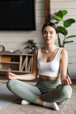 Farkındalık ve meditasyon kavramı. Genç Asyalı kadın evde egzersiz yapıyor. Oturma odasında yoga meditasyonu yapıyor.