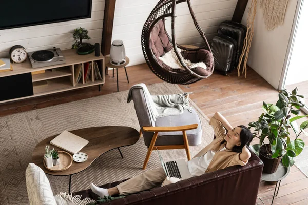 Sıcak hafta sonları. Mutlu, rahat Asyalı kadın evinde kanepede uzanıyor ve laptopunu kullanıyor, gözleri kapalı gülümsüyor.