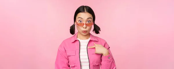 Close up retrato de menina asiática parece surpreso, aponta para si mesma com descrença, sendo escolhida, fica sobre fundo rosa — Fotografia de Stock