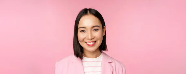 Nahaufnahme Porträt einer asiatischen Corporate Frau, die professionell aussieht, in die Kamera lächelt, Anzug trägt, vor rosa Hintergrund steht — Stockfoto