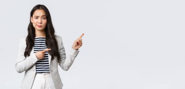 İş, finans ve istihdam, başarılı kadın girişimciler konsepti. Şüpheci ve tereddütlü Asyalı genç iş kadını bu tanıtıma güvenme, sırıtma ve sağ üst köşeyi işaret et.