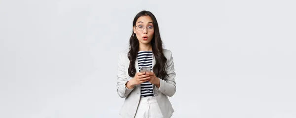 Business, finance and employment, female successful entrepreneurs concept. Surprised asian businesswoman in glasses and suit react astonished, holding mobile phone — Stock Photo, Image