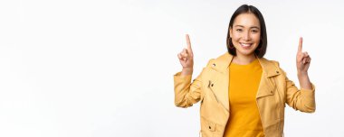 Hevesli Asyalı kız parmaklarını havaya kaldırıyor, üstte reklamını gösteriyor, mutlu bir şekilde gülümsüyor, tanıtım teklifi ya da afiş sunuyor, beyaz arka planda duruyor.