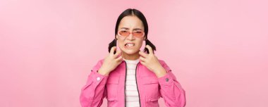 Image of angry, pissed off korean adult female model, shaking fists and shouting, screaming outraged, standing over pink background