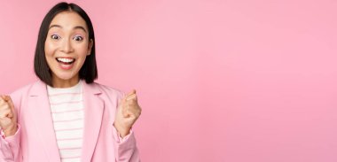 Hevesli satıcı, Asyalı kurumsal kadın evet diyor, hedefe ulaş ve kutla, zafer kazan, neşeyle bak ve gülümse, pembe arka planda dur.
