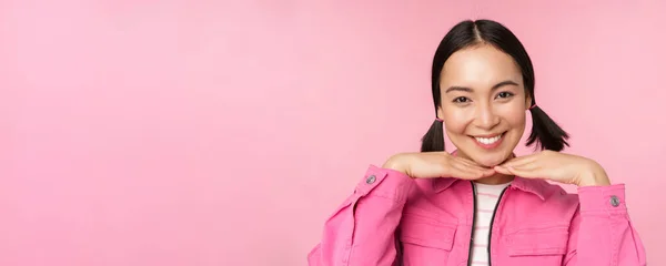 Концепция ухода за кожей и косметологии. Красивая азиатская девушка улыбается и смеется, показывая чистую здоровую кожу лица, позируя на розовом фоне — стоковое фото