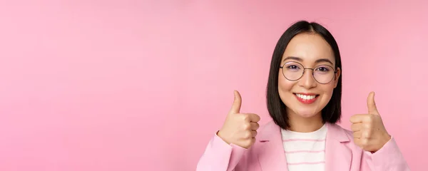 Impresionante, felicidades. Rostro de mujer de negocios asiática excitada en gafas, sonriendo complacido, mostrando los pulgares hacia arriba en la aprobación, de pie sobre fondo rosa —  Fotos de Stock