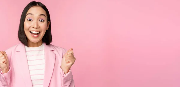 Захоплена продавчиня, азіатська корпоративна жінка каже "так", досягає мети і святкує, тріумфує, дивлячись з радістю і посмішкою, стоїть над рожевим тлом — стокове фото
