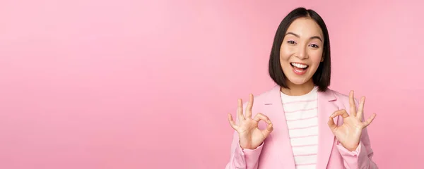 De acuerdo, excelente. Mujer de negocios en traje corporativo, mostrando ok, gesto de aprobación, recomendando smth, dar retroalimentación positiva y sonriendo complacido, posando sobre fondo rosa — Foto de Stock