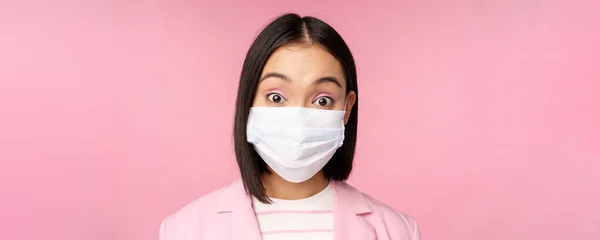 Primo piano ritratto di donna d'affari asiatica in maschera medica, guardando sorpreso, in piedi in abito su sfondo rosa — Foto Stock