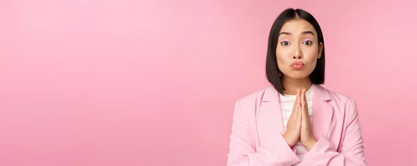 Ritratto di donna d'affari asiatica che chiede aiuto, diciamo per favore, in piedi in preghiera, in posa implorante, sfondo rosa dello studio — Foto Stock