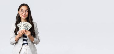 İş, finans ve istihdam, girişimci ve para kavramı. Hayalperest iş kadını nereye tatile gideceğini düşünüyor ve nasıl para kazanacağını düşünüyor, nakit tutuyor ve düşünceli bir iş kadını arıyor.