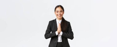 Siyah takım elbiseli, mutlu Asyalı iş kadını kibarca selamlıyor ve namaste diyor, müşterileri selamlıyor ve dostça gülümsüyor. Minnettar bayan yönetici yardımları için teşekkür ediyor, minnettar oluyor, yardımları takdir ediyor.