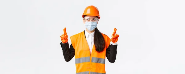 Covid-19肠胃安全规程，构建和预防病毒概念。满怀希望、乐观的亚洲女工程师头戴头盔和面罩，许愿，满脸喜色，双手交叉 — 图库照片
