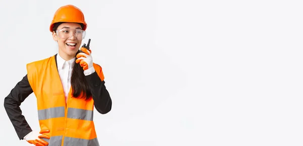 Confiante satisfeito asiático engenheiro feminino em capacete de segurança e uniforme falando com arquiteto-chefe usando walkie-talkie. Equipe de contato técnica de construção satisfeita usando telefone de rádio — Fotografia de Stock