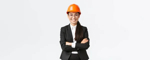 Professionell lächelnde asiatische Geschäftsfrau in Schutzhelm und Anzug, die selbstbewusst wirkt und Neubauten verkauft. Bauleiter, Ingenieur zeigt sich, grüßt Investoren — Stockfoto