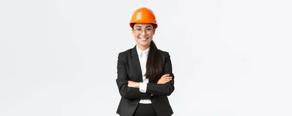 Professionele glimlachende Aziatische zakenvrouw in veiligheidshelm en pak cross arms en op zoek naar vertrouwen, de verkoop van nieuwe gebouwen. Bouwmanager, ingenieur die rondloopt, begroetende investeerders — Stockfoto