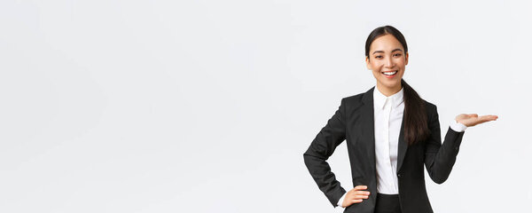 Professional smiling businesswoman introduce her project during meeting. Saleswoman in black suit holding hand right as showing product, holding on palm over blank white background