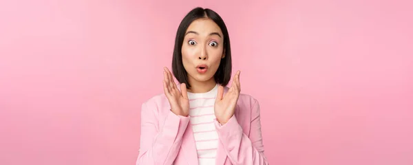 Retrato de mulher de negócios asiática olhando surpreso para a câmera, batendo palmas e olhando animado, sorrindo, posando contra fundo rosa — Fotografia de Stock