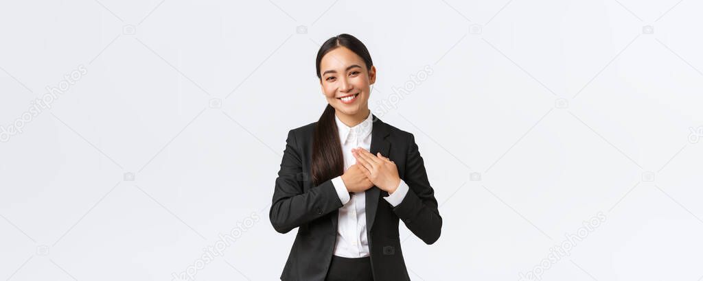 Happy pleased asian female entrepreneur love her clients, feeling flattered as receive praises with great job, holding hands on heart and smiling thankful, being grateful and appreciate efforts