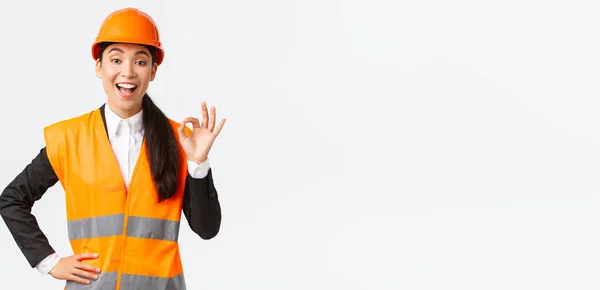 Tevreden tevreden Aziatische vrouwelijke ingenieur, bouwmanager in veiligheidshelm en reflecterende jas tonen oke gebaar blij, garanderen bouwkwaliteit, zorgen voor alles uitstekend — Stockfoto