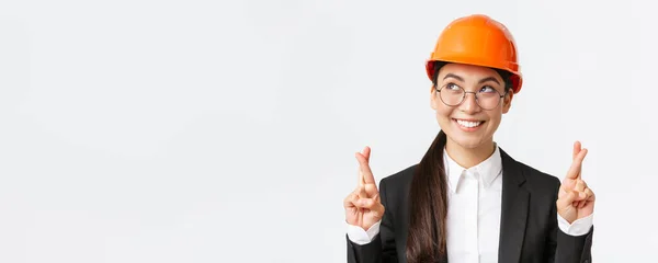 Close-up de esperançoso otimista asiático engenheiro feminino, arquiteto ter fé no projeto, vestindo capacete de segurança e terno de negócios aguardando bons resultados, dedos cruzados boa sorte, fundo branco — Fotografia de Stock