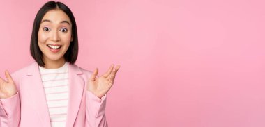 Asyalı iş kadınının portresi kameraya şaşırmış bakıyor, el çırpıyor, heyecanlı, gülümseyen pembe arka planda poz veriyor.