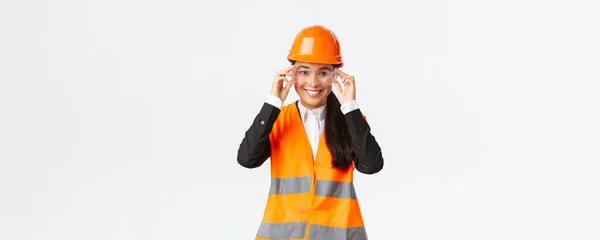 Jolie ingénieure asiatique souriante, gestionnaire de la construction en casque de sécurité et lunettes suivant le protocole avant d'entrer dans la zone du bâtiment ou l'entreprise, debout fond blanc — Photo