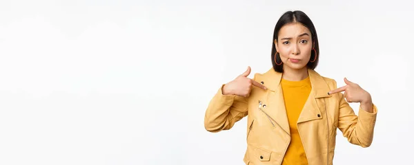 Imagem de unamused menina asiática apontando para si mesma, olhando com descrença cético para a câmera, posando contra fundo branco — Fotografia de Stock