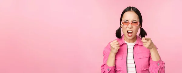 Image of angry, pissed off korean adult female model, shaking fists and shouting, screaming outraged, standing over pink background — Fotografia de Stock