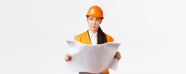 Réfléchi professionnel asiatique femme gestionnaire de la construction, architecte lecture des plans et regarder loin réfléchir, penser, prendre des décisions tout en étudiant le plan de projet, fond blanc — Photo