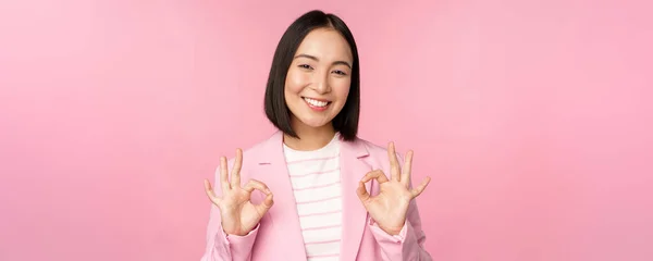 De acuerdo, excelente. Mujer de negocios en traje corporativo, mostrando ok, gesto de aprobación, recomendando smth, dar retroalimentación positiva y sonriendo complacido, posando sobre fondo rosa — Foto de Stock