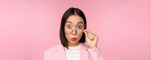 Primer plano retrato de la señora de la oficina coreana se quita las gafas y mirando impresionado a la cámara, expresión de la cara sorprendida, fondo rosa — Foto de Stock