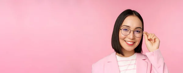 Successo asiatico donna d'affari in occhiali, sorridente e guardando professionale a macchina fotografica, indossando abito, in piedi su sfondo rosa — Foto Stock