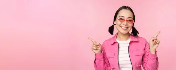 Choice. Stylish korean girl, asian female model points fingers sideways, shows two variants, product advertisement, demonstrating items, standing over pink background — Stock Photo, Image
