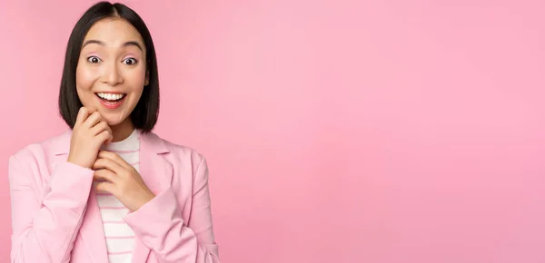 Joyeux jeune femme de bureau, femme d'affaires coréenne portant un costume, regardant surpris par la caméra, posant sur fond de studio en rose — Photo