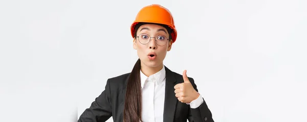 Close-up of professional pleased asian female chief engineer, architect in business suit and safety helmet showing thumbs-up in approval, give permission, recommend construction company — Stock Photo, Image