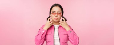 Image of angry, pissed off korean adult female model, shaking fists and shouting, screaming outraged, standing over pink background