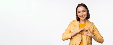 Asyalı güzel bir kızın görüntüsü kalp, aşk işareti, özen ve romantik duygular gösteriyor, beyaz stüdyo arka planında duruyor.