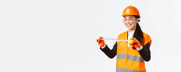 Agradado sorrindo asiático arquiteto feminino conseguir bons resultados, olhando satisfeito em fita métrica depois de medir layout na área de construção, de pé em capacete de segurança e roupas reflexivas — Fotografia de Stock