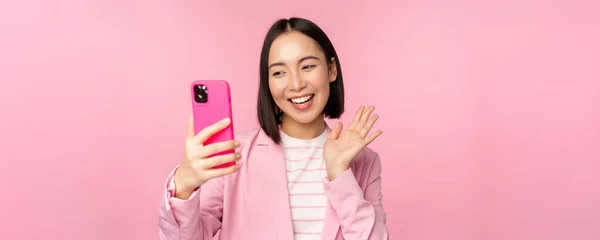 Snygg asiatisk affärskvinna, flicka i kostym tar selfie på smartphone, videochatt med mobiltelefon app, poserar mot rosa studio bakgrund — Stockfoto