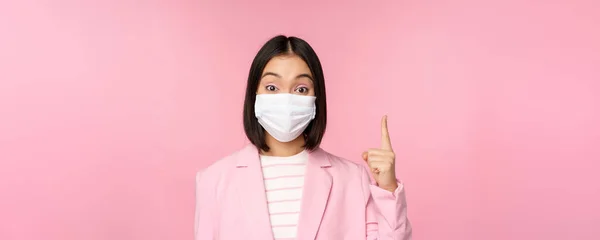 医師の顔のマスクとスーツでアジアの実業家の肖像画を閉じる,指を指して,広告を表示,トップバナー,ピンクの背景の上に立って — ストック写真