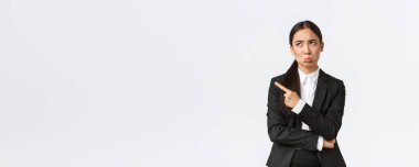 Üzgün ve hayal kırıklığına uğramış kadın girişimci, takım elbiseli komisyoncu, somurtkan, hoşnutsuz ve üzgün görünüyor ve sol üst köşeyi işaret ediyor, tedirgin, beyaz arka plan