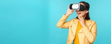 VR kulaklık takan mutlu Asyalı kadın modelin portresi. Sanal gerçeklik gözlükleriyle gülüyor ve gülümsüyor. Mavi arka planda duruyor.