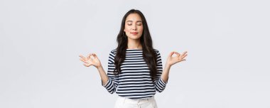 Yaşam tarzı, insanların duyguları ve gelişigüzel kavramlar. Sakin ve sabırlı gülümseyen, gözleri kapalı Asyalı bir kadın sakinleşmek için meditasyon yapıyor, elleri zen hareketiyle nefes egzersizleri yapıyor.
